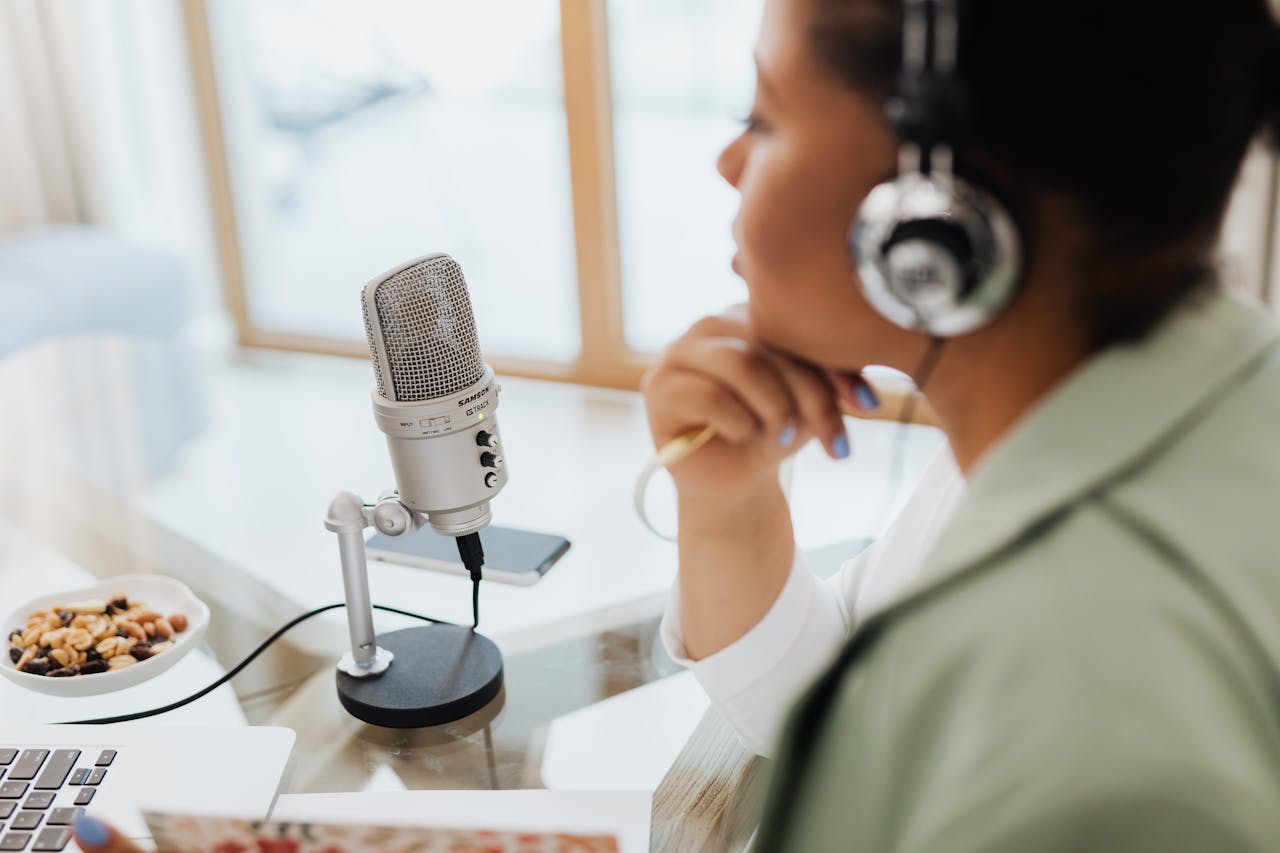 Woman using laptop and microphone for podcasting at home.